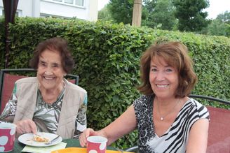 Zwei lächelnde Frauen am Gartentisch mit Tassen und Teller