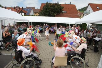 Ältere Menschen in Rollstühlen unter Pavillons wedeln bunte Tücher im Kreis
