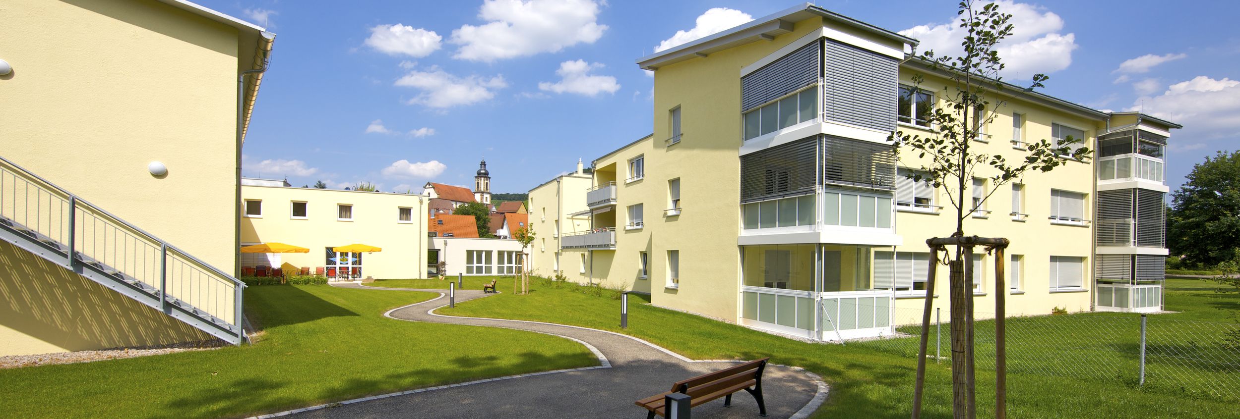 Gelbe Mehrfamilienhäuser mit geschwungenem Weg, Bänken und Grünfläche