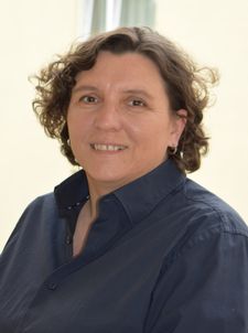 Lächelnde Person mit kurzen Locken und dunklem Hemd auf Balkon